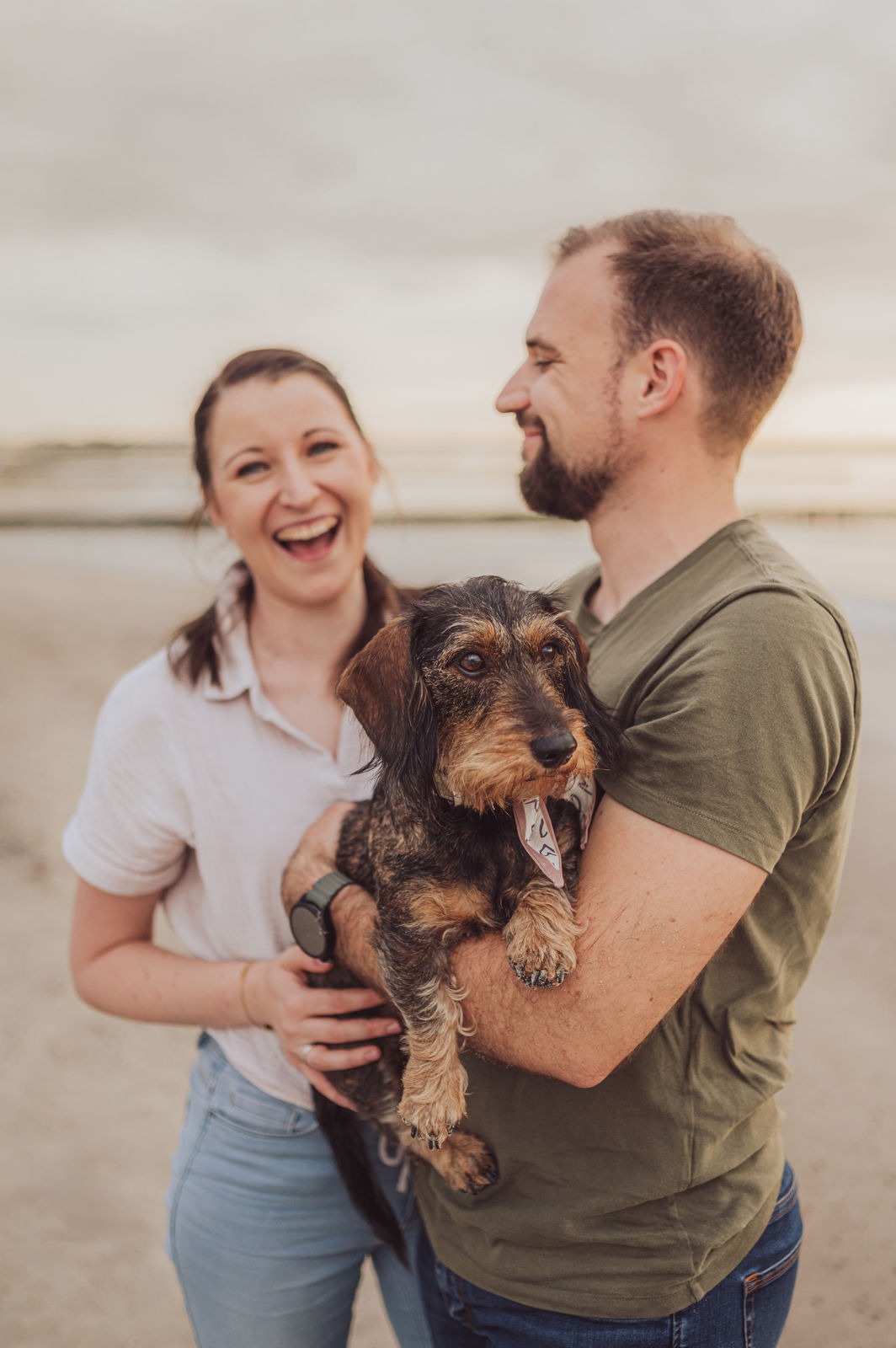 Paar lacht mit Rauhaardackel auf dem Arm beim Hundeshooting Markgrafenheide Hundefotografin Rostock